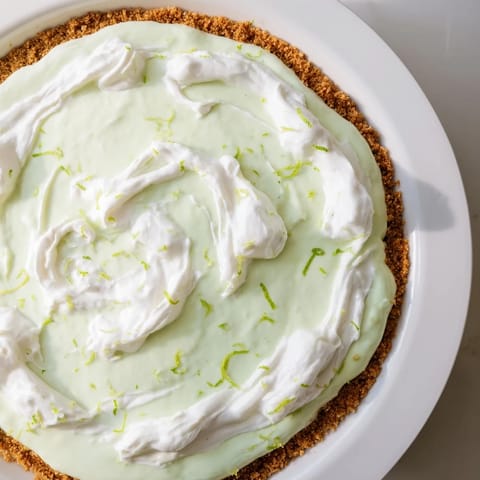 A slice of creamy key lime pie, topped with fluffy whipped cream and lime zest.