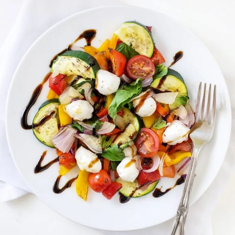 Fresh mozzarella pearls and torn basil leaves sprinkled over warm roasted vegetables, ready to be served as a vibrant side dish.