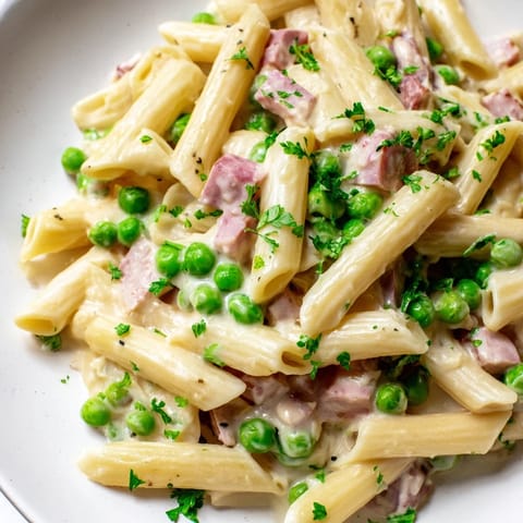 Spring Pea & Ham Pasta served warm in a skillet, featuring tender penne coated in cream with bright green peas.