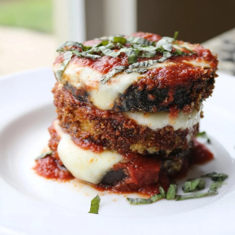A close-up of Eggplant Parmesan shows crispy baked eggplant and layers of cheese in a baking dish.