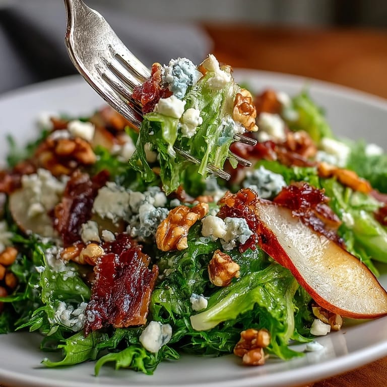 Fresh frisée lettuce topped with sweet pear slices, creamy blue cheese, toasted walnuts, and savory prosciutto in a colorful bowl.