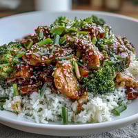 A close-up of One Pan Honey Garlic Chicken Broccoli Rice, featuring golden chicken pieces and bright green broccoli florets nestled in fluffy white rice.  